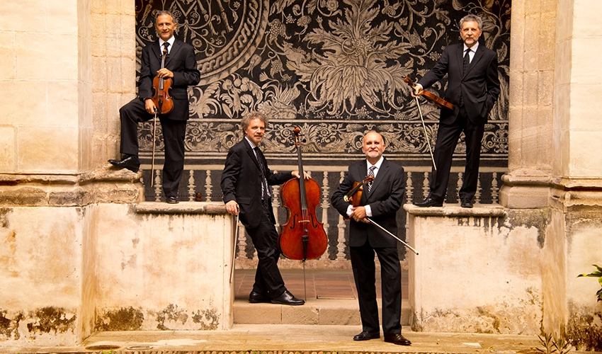 photo of four musicians holding their string instruments standing in a "U" formation on some steps outside an old building with columns